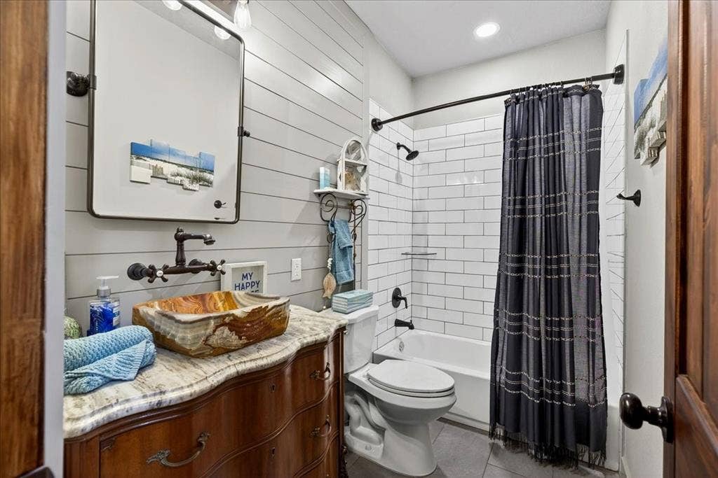 11591 Farm Market 59, Athens, TX 75751 Hallway Bathroom on Level 1 featuring a unique natural stone vessel sink, wall-mounted faucet, and a vanity with a light-colored countertop, shiplap accent wall, subway tile in tub/shower, gray tile floor.