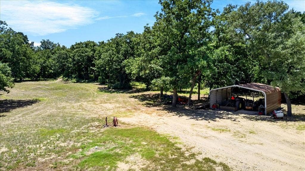 11591 Farm Market 59, Athens, TX 75751 Expansive clearing surrounded by mature trees, featuring a gravel driveway and a 2-car carport.