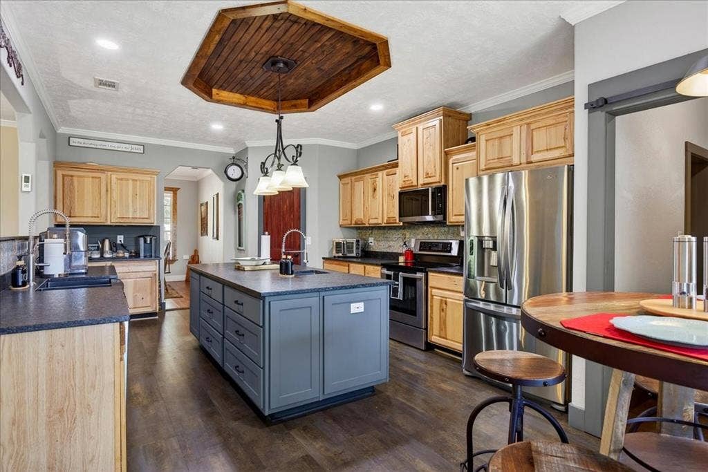 11591 Farm Market 59, Athens, TX 75751 Spacious kitchen featuring a central island with integrated storage, wood-finish flooring, recessed lighting, and a wood-paneled ceiling accent. Open to the living, granite counters, pine cabinets, tile back splash, double black metal farm sink, coffee bar with small sink, large pantry and breakfast area.