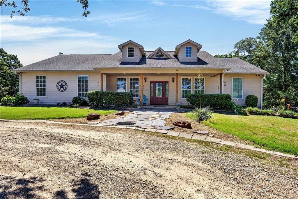 11591 Farm Market 59, Athens, TX 75751 Ranch-style residence featuring a covered front porch with natural wood columns, a red entry door, multiple dormer windows, and a flagstone pathway