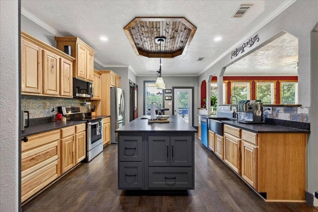 11591 Farm Market 59, Athens, TX 75751 Spacious kitchen featuring natural wood cabinetry, dark countertops, wood-finish flooring, a central island with a contrasting dark finish, and a wood-paneled tray ceiling, granite counters, pine cabinets, tile back splash, double black metal farm sink.