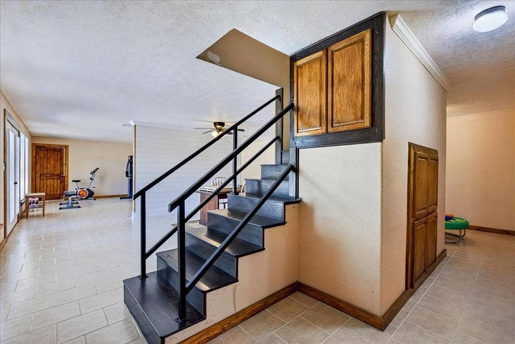 11591 Farm Market 59, Athens, TX 75751 WOW - fully air conditioned basement add another 1565SF. Open-concept interior featuring a prominent staircase with black metal railings, wood-finish treads, and integrated under-stair cabinetry, large open spaces on each side of staircase, a full bathroom, utility room, and 2 more bedrooms, French doors lead outside.