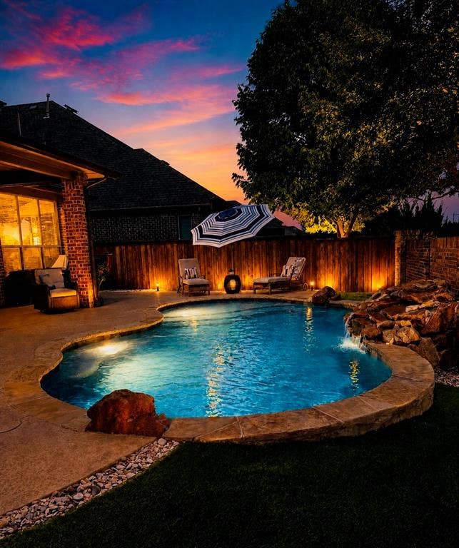 6905 Denali Drive, McKinney, TX 75070 Freeform swimming pool with integrated rock waterfall feature, ambient landscape lighting, concrete decking, and a privacy fence