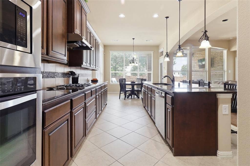 6905 Denali Drive, McKinney, TX 75070 Kitchen featuring dark wood cabinetry, black countertops, stainless steel appliances, and tile flooring