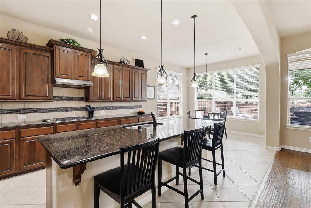 6905 Denali Drive, McKinney, TX 75070 Kitchen featuring wood cabinetry, dark countertops, tile flooring, pendant lighting, and multiple windows
