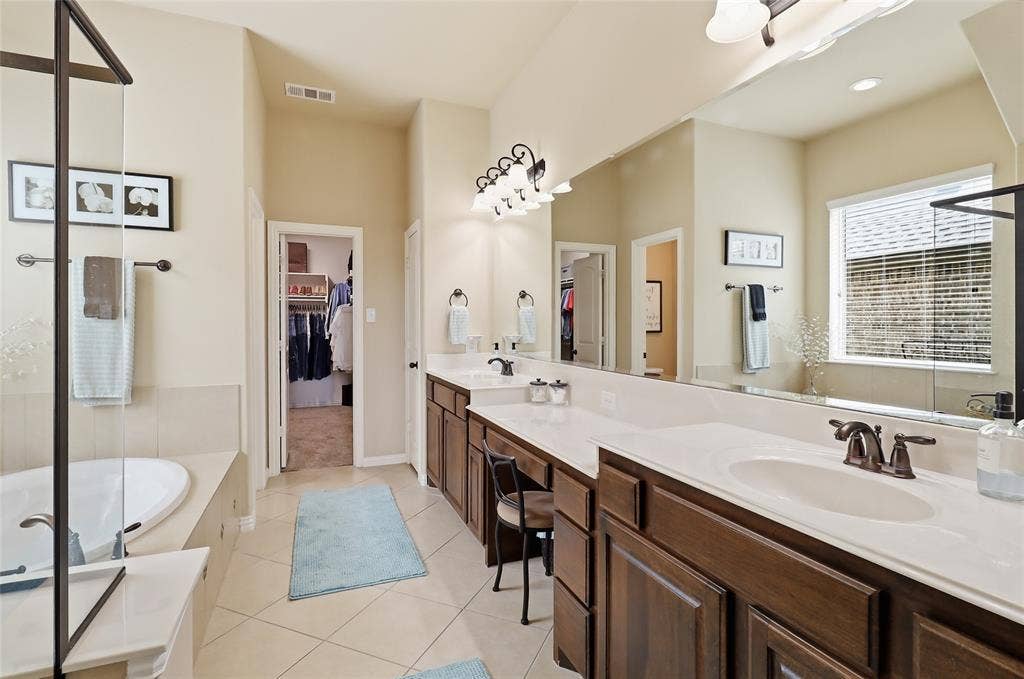 6905 Denali Drive, McKinney, TX 75070 Bathroom featuring a dual vanity with white countertops and dark wood cabinetry, a built-in soaking tub, a separate glass-enclosed shower, and tile flooring