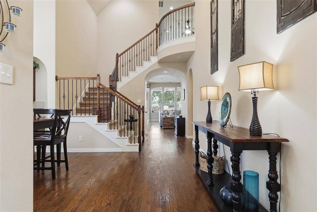 6905 Denali Drive, McKinney, TX 75070 Two-story foyer featuring wood-finish flooring, a grand staircase with wrought iron balusters and wood handrails, and arched doorways
