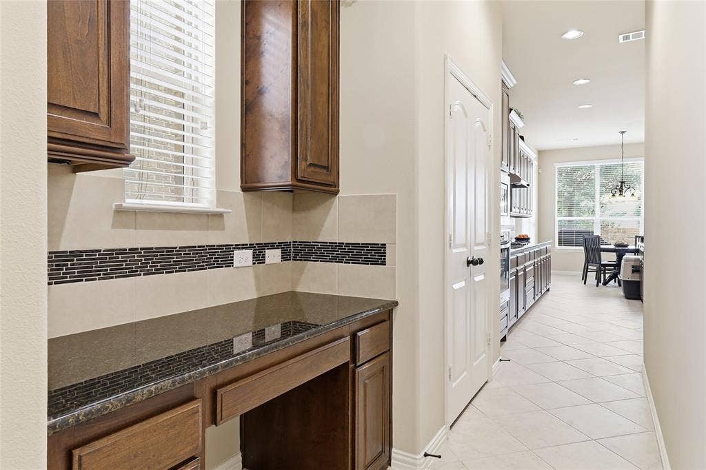 6905 Denali Drive, McKinney, TX 75070 Built-in desk area featuring wood cabinetry, a dark countertop, and a tiled backsplash with a decorative mosaic accent