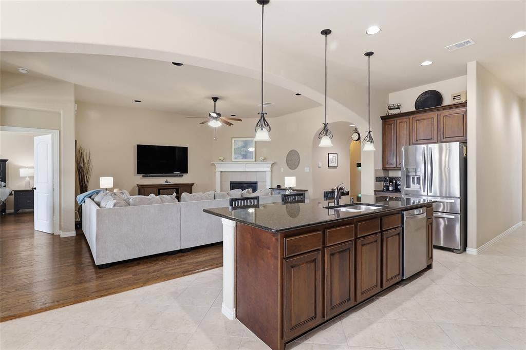 6905 Denali Drive, McKinney, TX 75070 Kitchen with dark wood cabinetry, stainless steel appliances, and a central island featuring a sink and pendant lighting