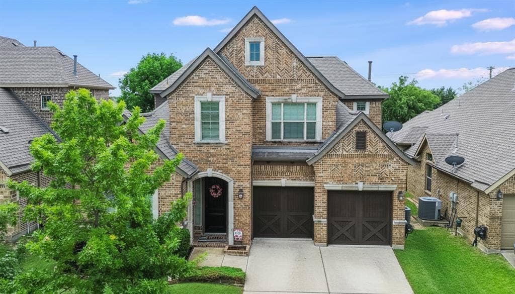 6905 Denali Drive, McKinney, TX 75070 Brick exterior featuring a two-car garage, prominent gabled rooflines, arched entry, and a dormer window