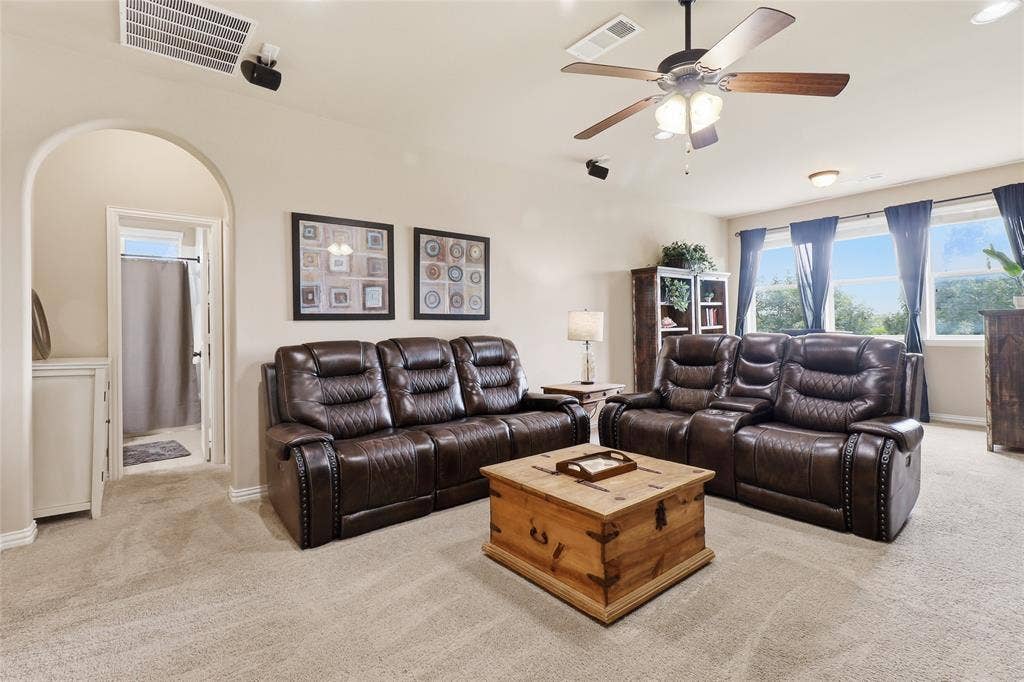 6905 Denali Drive, McKinney, TX 75070 Spacious carpeted room featuring a ceiling fan with integrated lighting, recessed overhead speakers, multiple windows, and an arched doorway
