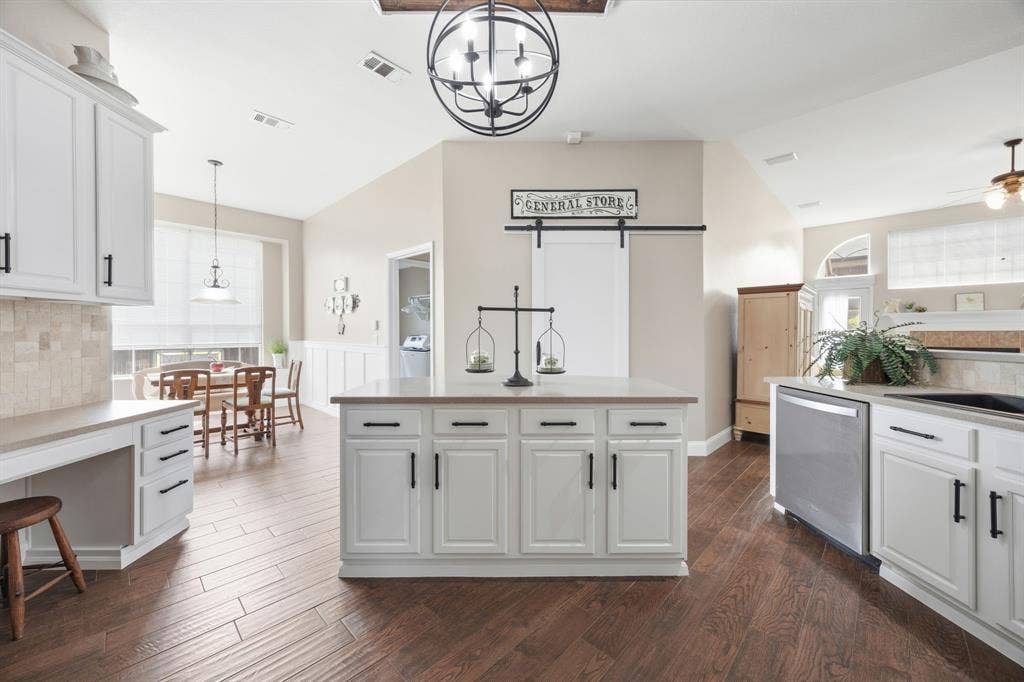 Spacious kitchen featuring white cabinetry, a central island with a light-colored countertop, dark wood-finish flooring, and stainless steel appliances