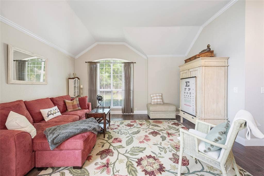 Vaulted ceilings with crown molding, arched window with grid pattern, wood-finish flooring, and neutral wall tones