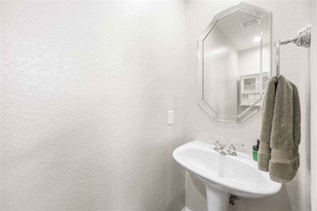 White pedestal sink with chrome faucet, octagonal framed mirror, and chrome towel bar