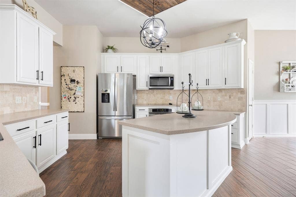 Bright kitchen featuring white cabinetry, light countertops, stainless steel appliances, a tile backsplash, and wood-finish flooring