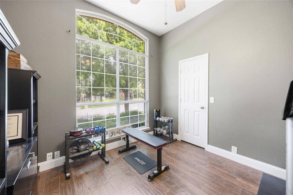 Room featuring a large arched window with grid patterns, wood-finish flooring, a paneled door, and a ceiling fan