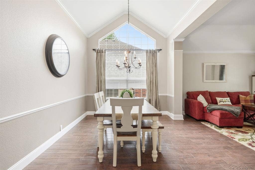 Dining area featuring vaulted ceilings, a large arched window with blinds and drapery, wood-finish flooring, a chandelier, and a chair rail with picture frame molding