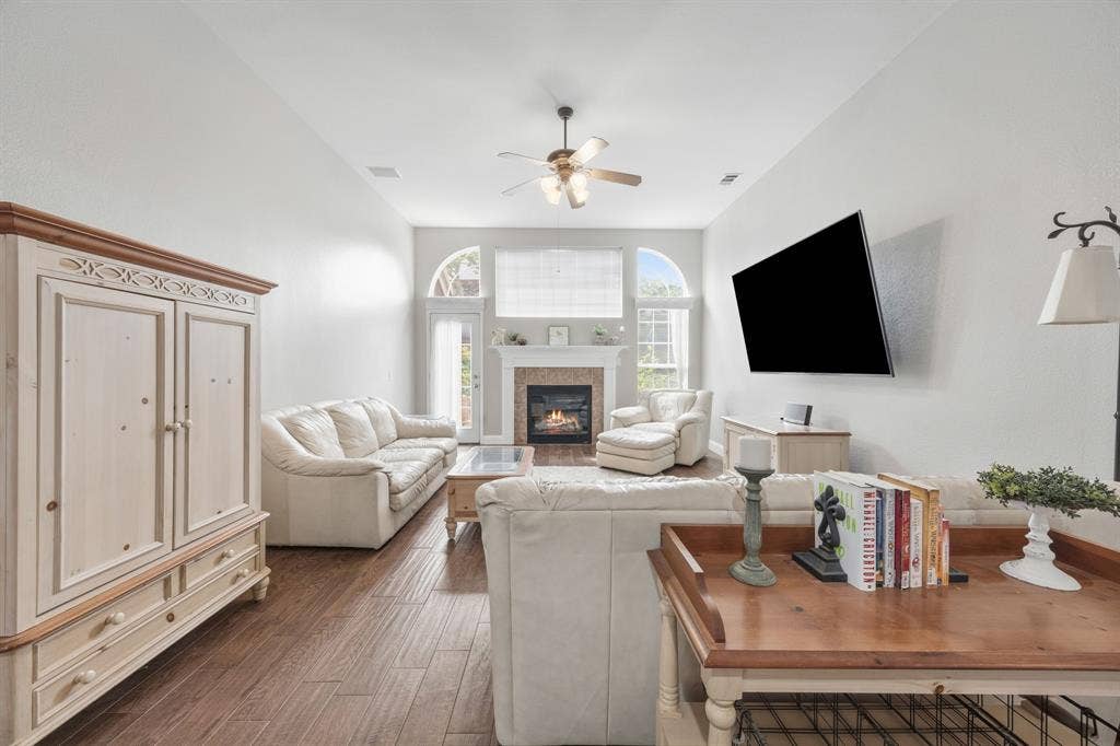 Spacious living area featuring wood-finish flooring, a fireplace with a stone surround and mantel, arched windows, and vaulted ceilings
