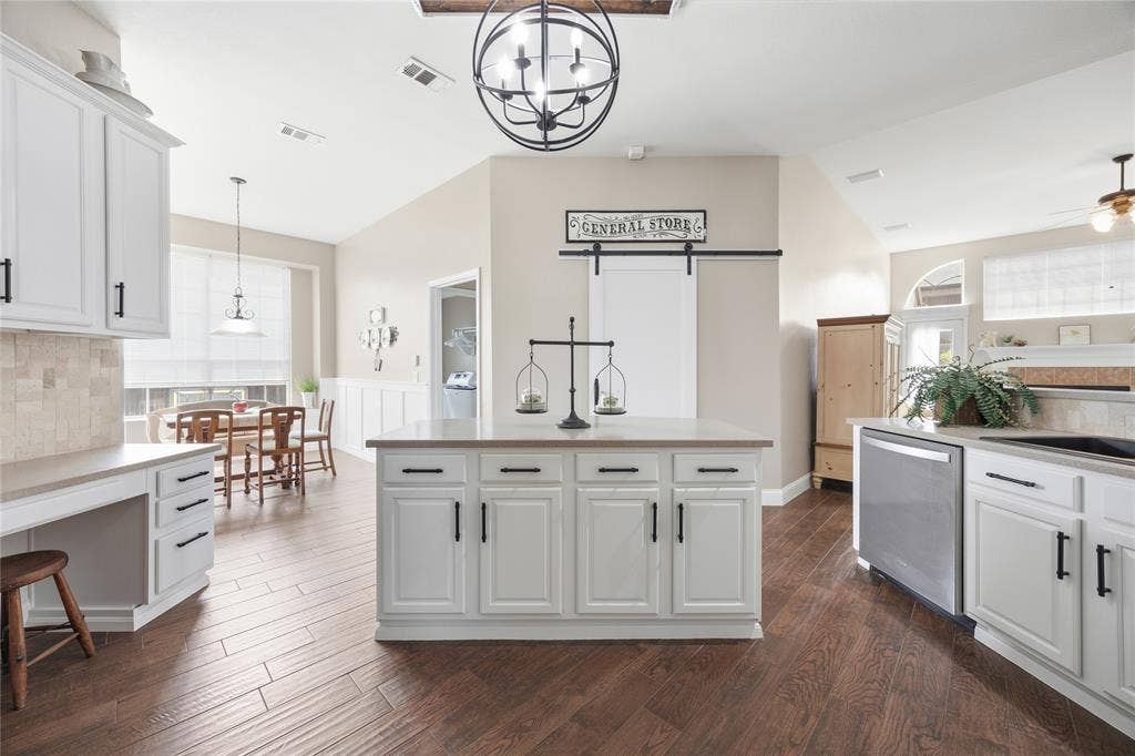 Kitchen featuring a central island with white cabinetry, wood-finish flooring, stainless steel dishwasher, vaulted ceiling with a spherical chandelier, and a barn door
