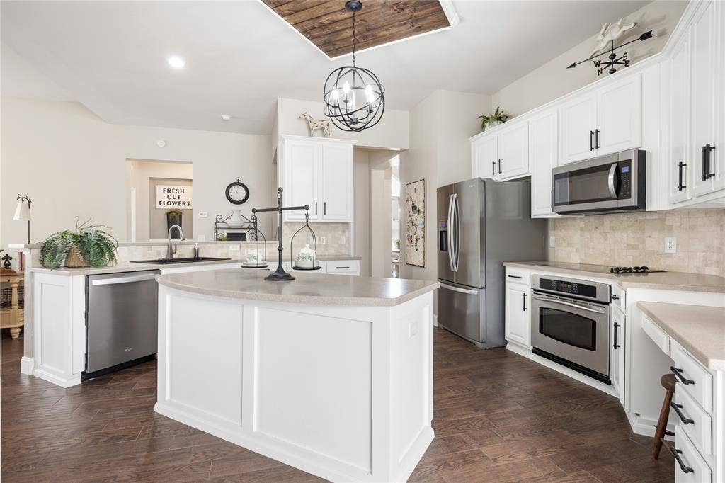 Kitchen featuring a central island, white cabinetry, integrated stainless steel appliances, wood-finish flooring, and a unique wood-paneled ceiling accent