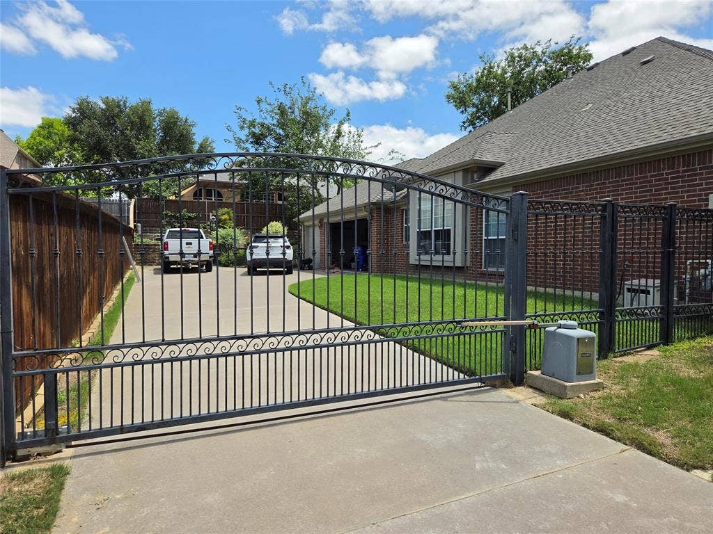 Wrought iron gate entry with an automatic opener, concrete driveway, and mature landscaping