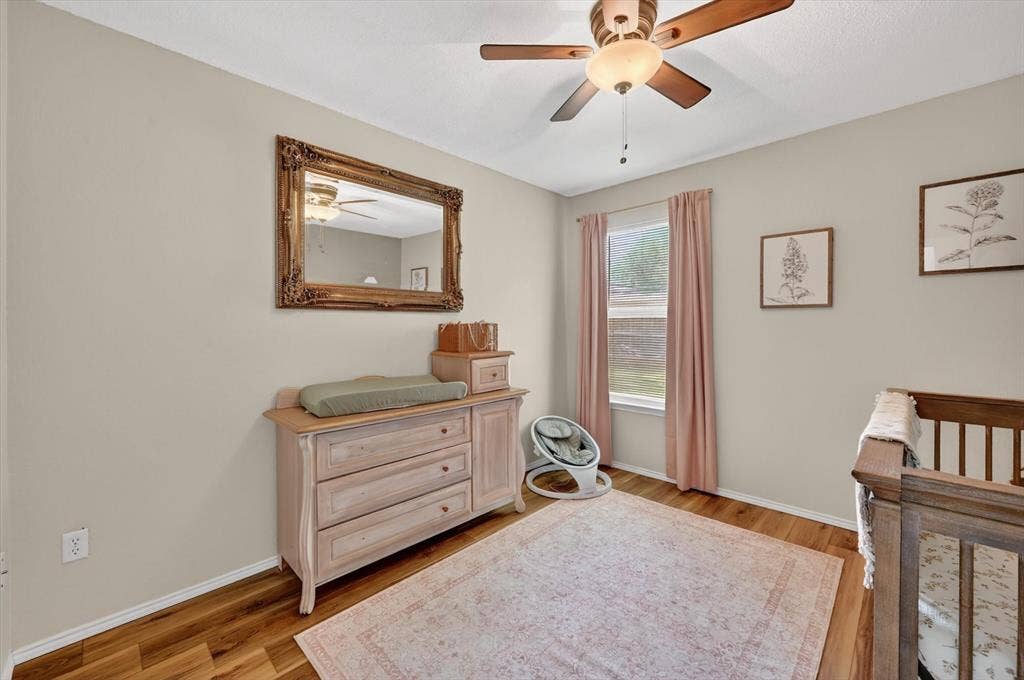 Room featuring wood-finish flooring, a ceiling fan with integrated lighting, and a single window with vertical blinds