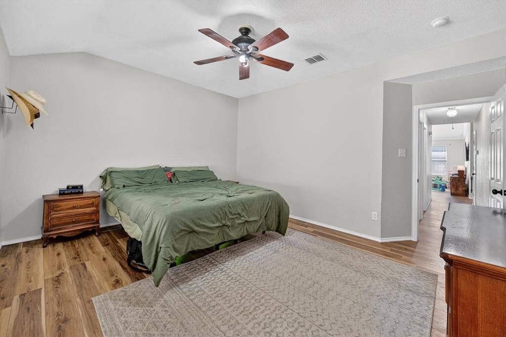 Spacious room featuring wood-finish flooring, a ceiling fan with light fixture, and light gray wall paint