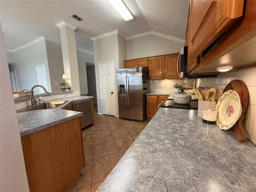 Kitchen with tile flooring, wood cabinetry, stainless steel appliances, and solid surface countertops