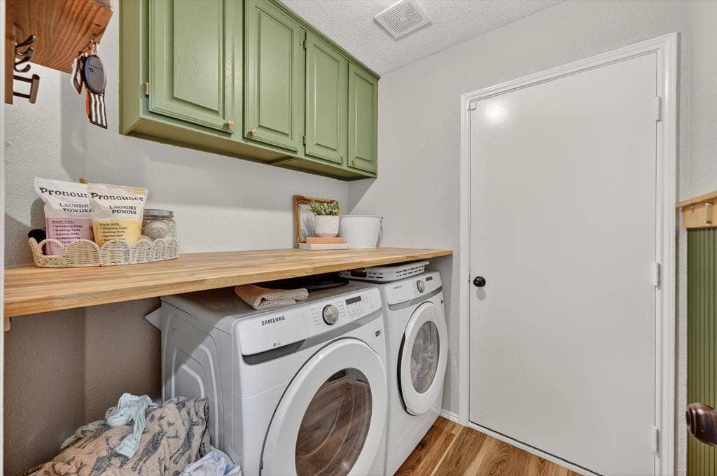 Laundry area featuring light wood-finish flooring, a white door with a black knob, and light green upper cabinetry