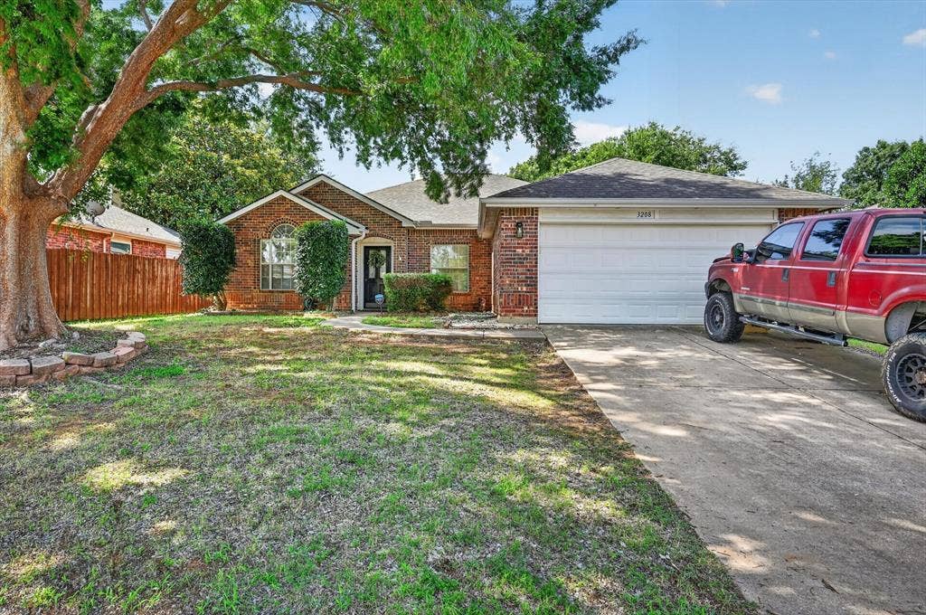 Traditional brick exterior residence featuring a mature shade tree, a concrete driveway, an attached garage, and a fenced backyard