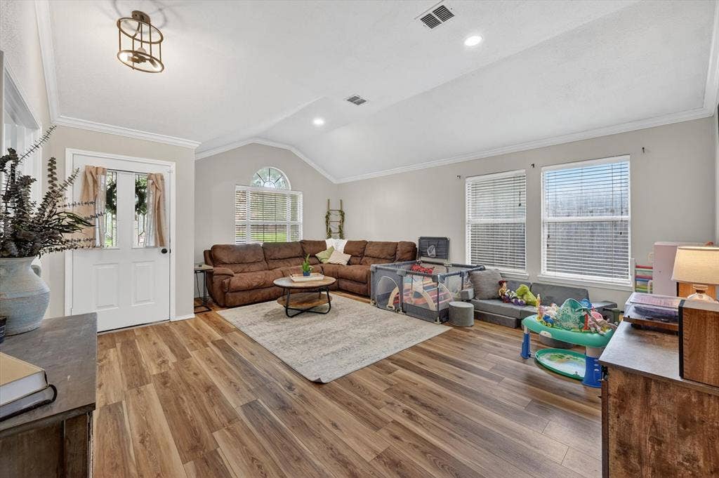 Spacious living area featuring wood-finish flooring, vaulted ceilings, and crown molding