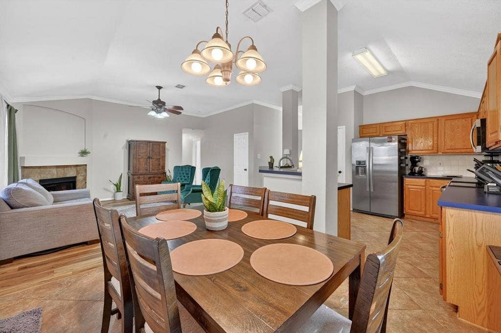 Open-concept dining area with wood-finish flooring, a contemporary chandelier, vaulted ceilings, and crown molding, offering direct sightlines to the kitchen and living room