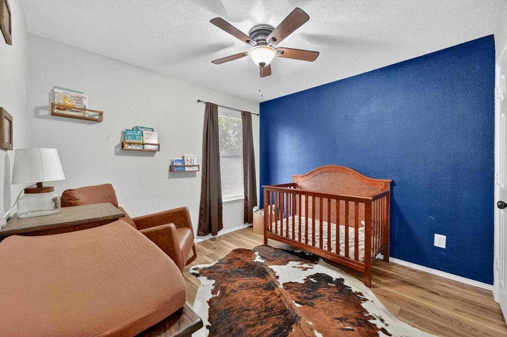 Room featuring wood-finish flooring, a ceiling fan with integrated lighting, and a window with dark curtain rods