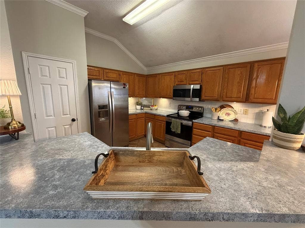 Vaulted ceiling, crown molding, wood cabinetry, white subway tile backsplash, and stainless steel appliances