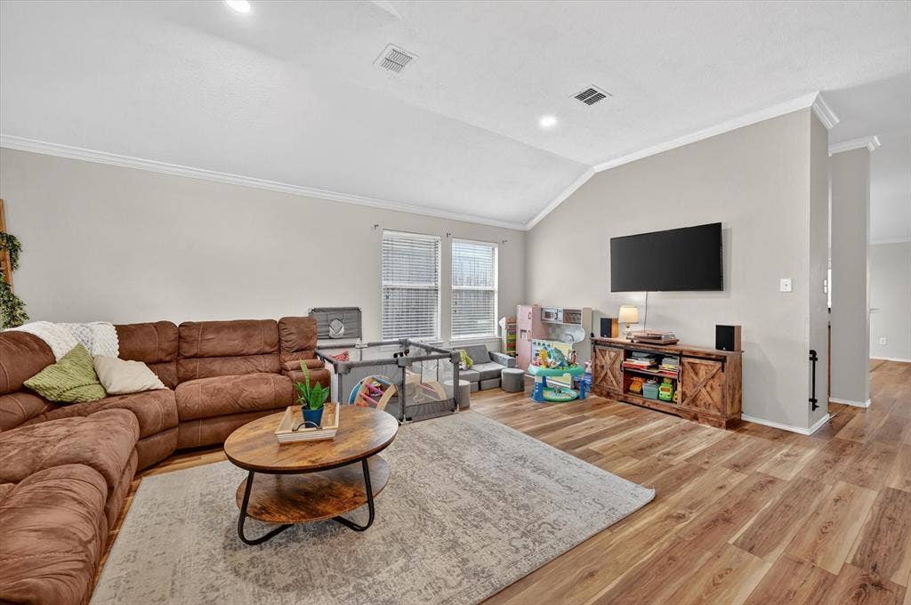 Spacious living area featuring vaulted ceilings, crown molding, wood-finish flooring, and recessed lighting