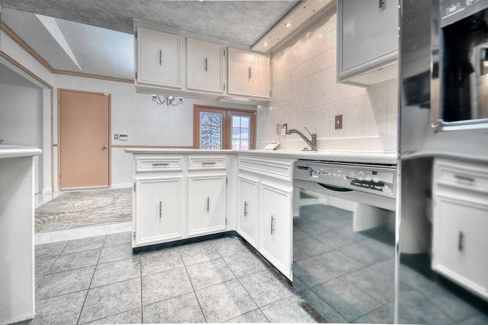 White cabinetry with silver hardware, light-toned countertop, stainless steel dishwasher, tile flooring, and a tiled backsplash