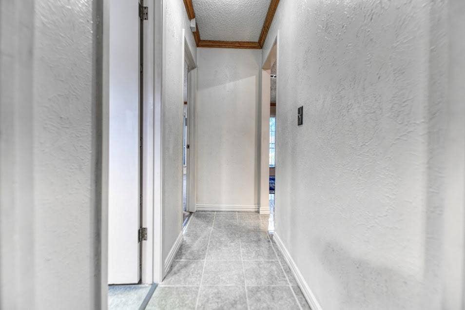 Hallway featuring textured white walls, light gray tile flooring, white trim, and a wood-finish ceiling accent