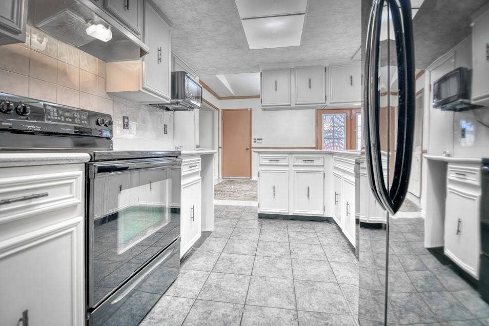 Kitchen featuring white cabinetry, tile flooring, black range, black microwave, and a window with decorative glass