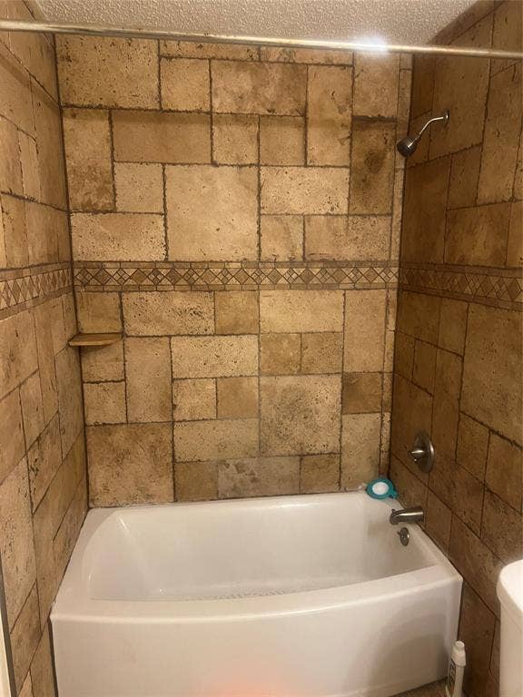 121 Brookside Drive, Duncanville, TX 75137 Bathtub and shower combination featuring earth-toned stone-look tile surround with decorative accent band and built-in shower shelf