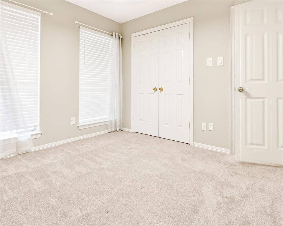 6005 Pin Oak Drive, McKinney, TX 75072 Carpeted room featuring two windows with white blinds and sheer curtains, a bifold closet, and a paneled door