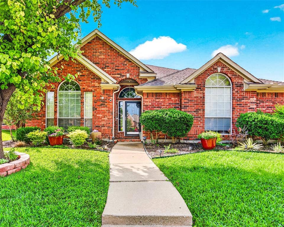 6005 Pin Oak Drive, McKinney, TX 75072 Brick facade residence featuring arched windows with grids, a prominent front entry with a glass-paneled door, and a concrete walkway