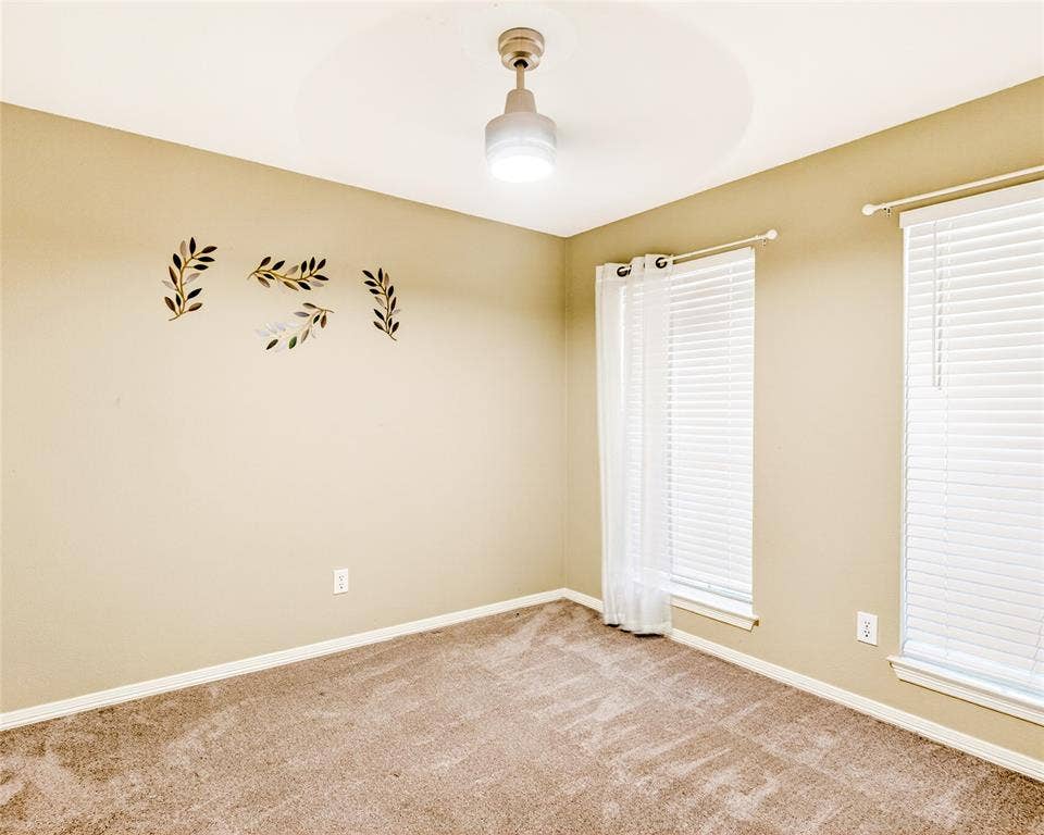 6005 Pin Oak Drive, McKinney, TX 75072 Carpeted interior room featuring two windows with white blinds and sheer curtains, a ceiling-mounted light fixture, and beige wall paint