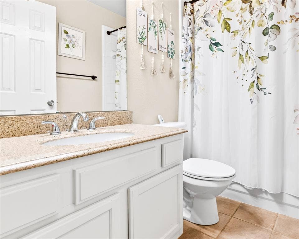 6005 Pin Oak Drive, McKinney, TX 75072 Bathroom featuring a light-colored vanity with panel detailing, a speckled countertop, an undermount sink with a chrome faucet, a white toilet, and neutral floor tiles