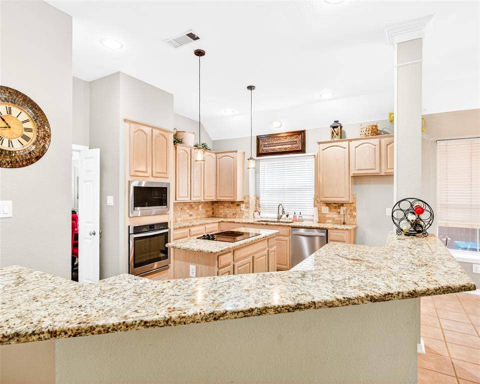 6005 Pin Oak Drive, McKinney, TX 75072 Kitchen featuring light wood cabinetry, stainless steel appliances, and a multi-toned backsplash