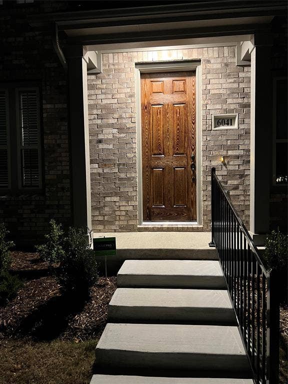 6041 Roper Road, McKinney, TX 75070 Entryway featuring a paneled wood-finish door, brick facade, concrete steps, wrought iron railing, and manicured landscaping
