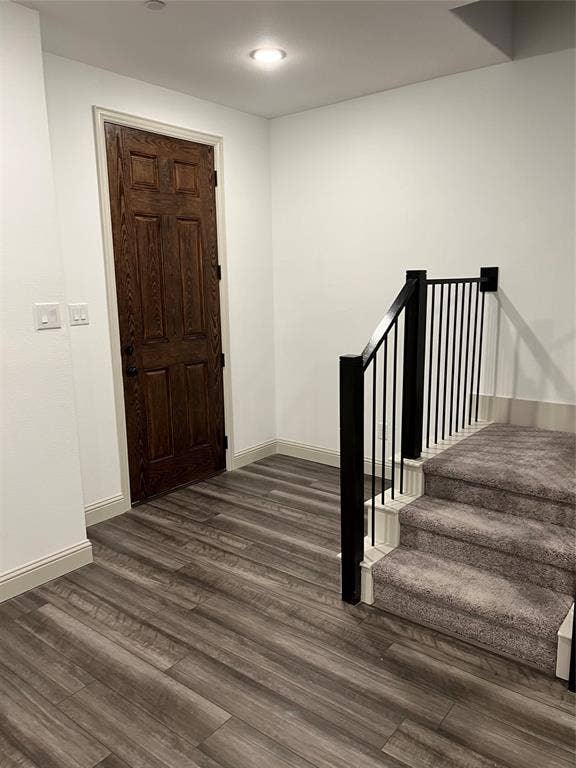 6041 Roper Road, McKinney, TX 75070 Entryway featuring wood-finish flooring, a dark wood paneled door, recessed ceiling lighting, and a carpeted staircase with a black metal railing