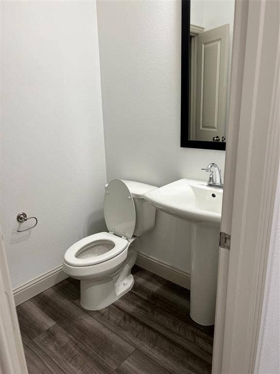 6041 Roper Road, McKinney, TX 75070 Compact powder room featuring a pedestal sink with a chrome faucet, a white toilet, wood-finish flooring, and a framed mirror