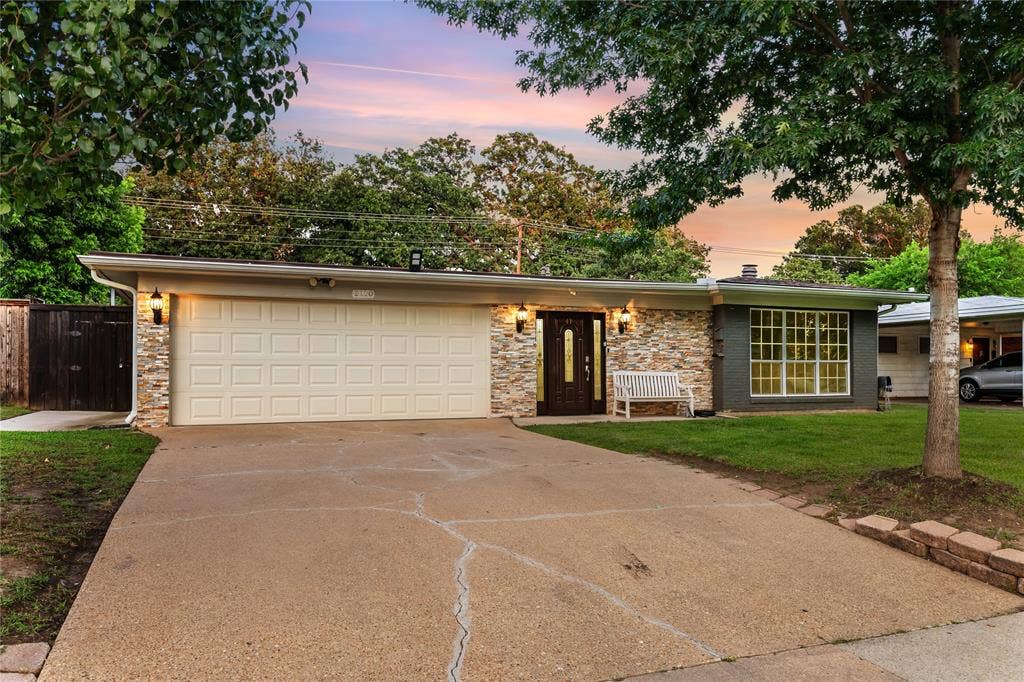 Ranch-style exterior with a two-car garage, stone facade accents, a dark wood-finish entry door, and a large front window with grid detailing