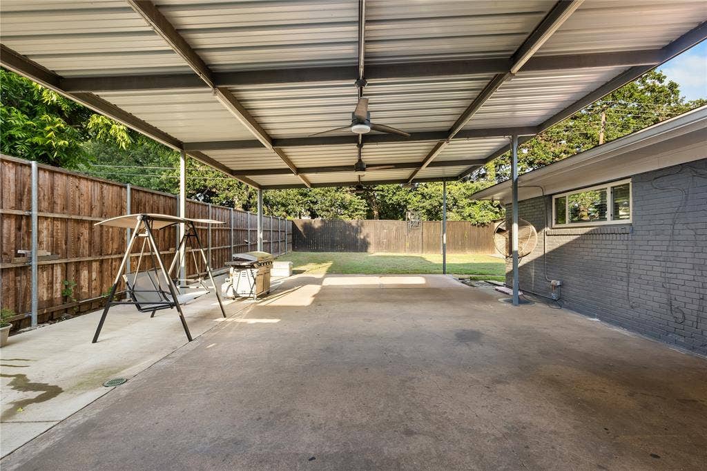 Expansive covered patio featuring a corrugated metal roof supported by metal beams, concrete flooring, and multiple ceiling fans