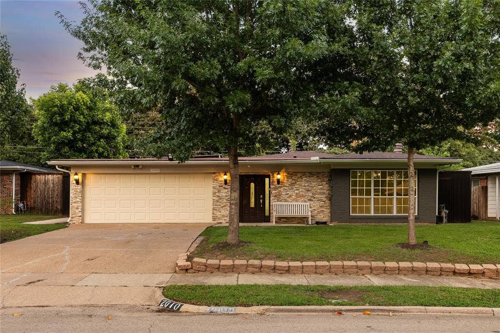 Single-story residence featuring a two-car garage with a paneled door, stone facade accents, and a contrasting dark gray exterior finish